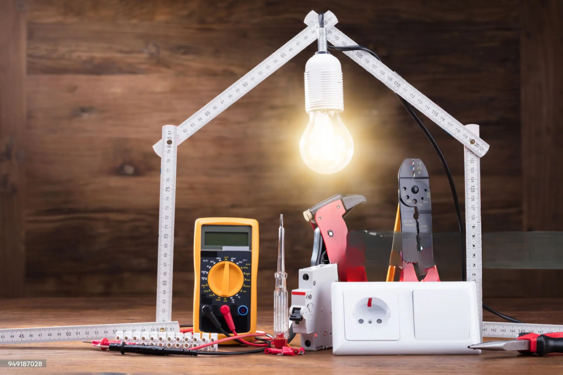 "Electrician smiling and installing an electrical panel with colorful wires, wearing a yellow hard hat and blue overalls in a construction environment."